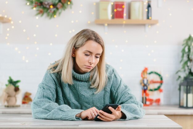 Piękna samotna kobieta z depresją pozostawiona sama w Wigilię, ze smutkiem patrząca na telefon