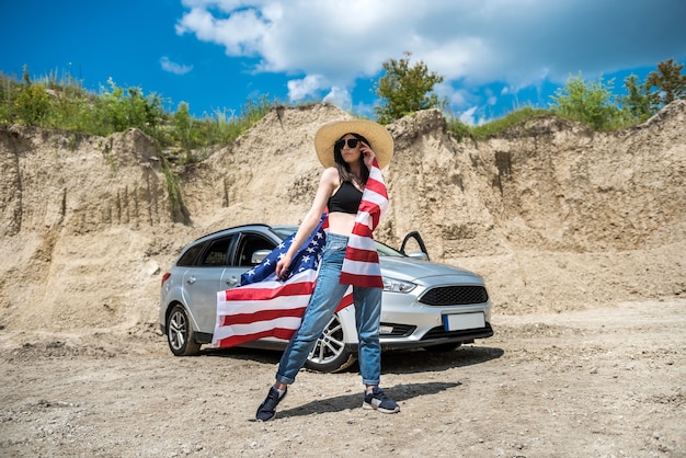 Piękna sexy dziewczyna z amerykańską flagą i okulary w pobliżu samochodu w kamieniołomie piasku. Letni dzień