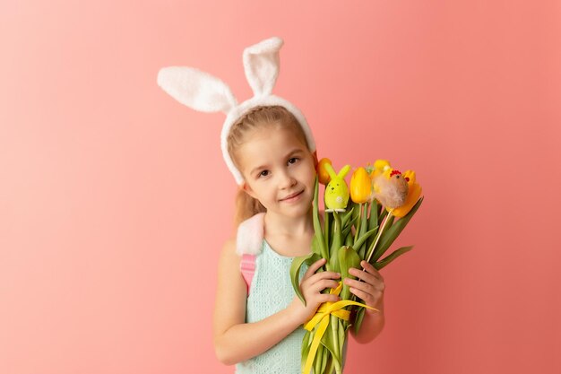 Piękna śliczna mała dziewczynka w uszach króliczka wielkanocnego uśmiecha się i trzyma wiosenny bukiet żółtych tulipanów