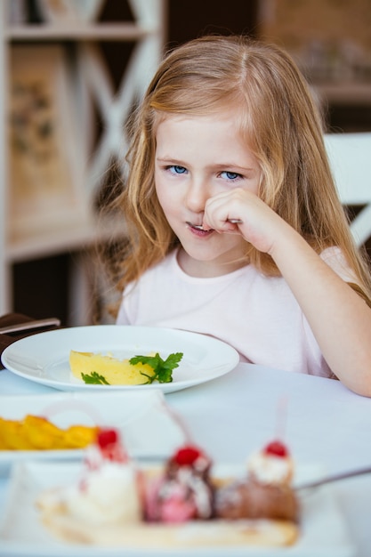 Zdjęcie piękna, śmiejąca się dziewczynka blondynka siedzi przy stole w kawiarni i zjadła tłuczone ziemniaki z talerza.