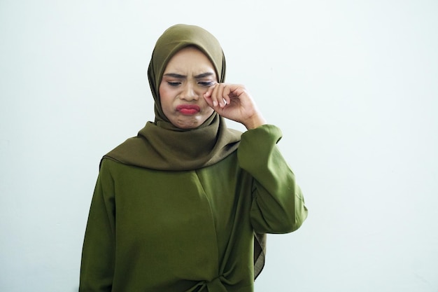 Piękna smutna młoda azjatycka muzułmanka ubrana w zieloną sukienkę i hidżab trzymająca oczy