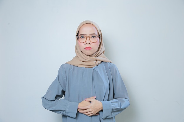 Piękna smutna młoda azjatycka muzułmańska biznesowa kobieta w okularach trzymająca brzuch