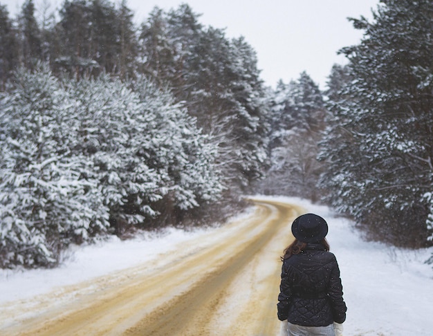 Piękna śnieżna zamieć Dziewczyna stoi plecami na środku drogi w gęstym sosnowym lesie Piękna droga