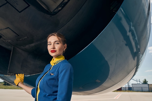 piękna spokojna młoda stewardessa oparta jedną ręką o silnik samolotu