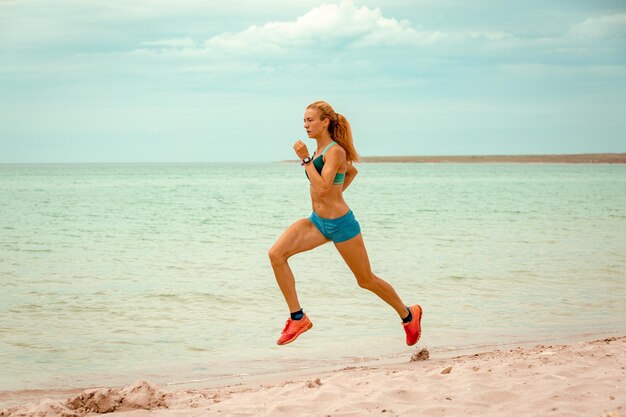 Piękna sportive kobieta biegnie wzdłuż pięknej, piaszczystej plaży, zdrowy styl życia, ciesząc się aktywnymi letnimi wakacjami w pobliżu morza