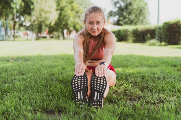 Piękna, sportowa kobieta z długimi włosami robi rozciąganie w parku przed joggingiem