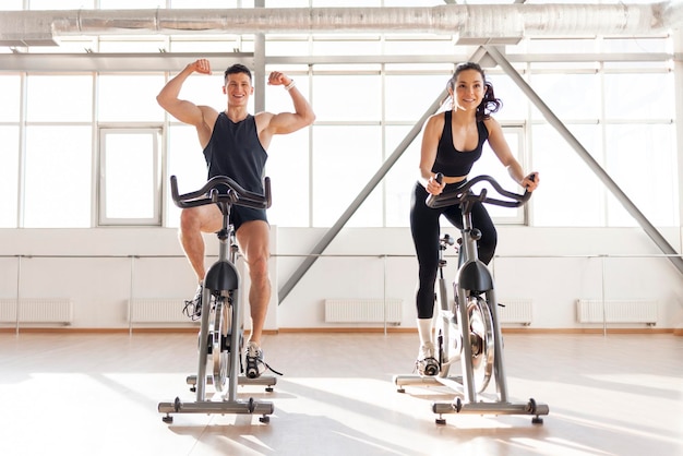 Piękna sportowa para rowerzystów trenuje w sali fitness na statycznym symulatorze rowerowym