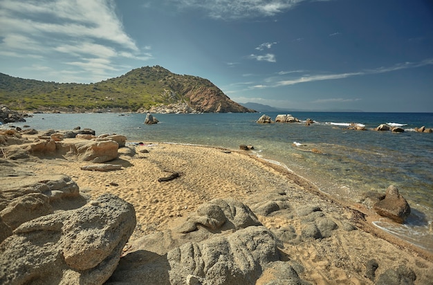 Piękna śródziemnomorska plaża typowa dla wybrzeża południowej Sardynii przejęta latem. Plaża, skały i góry za nimi łączą się w cudowną panoramę niesamowitego piękna.