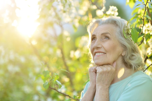 Piękna starsza kobieta pozuje w pobliżu kwitnącego drzewa