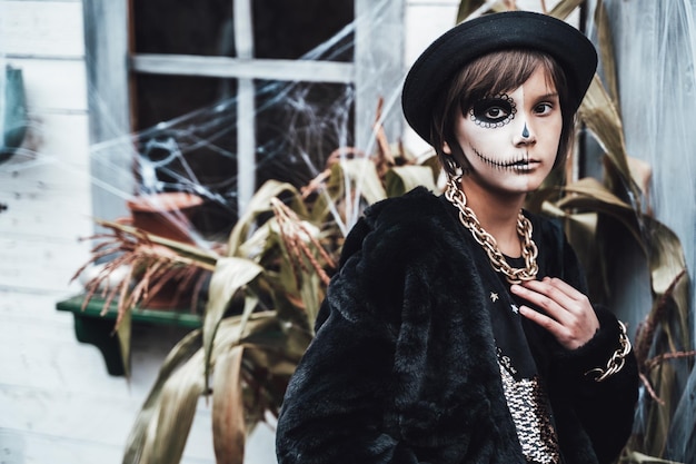 Piękna straszna dziewczynka świętuje halloween Przerażający czarny biały pół twarzy makijaż i strój czarownicy stylowy obraz Horror zabawa na imprezie dla dzieci w stodole na ulicy Łańcuch futra kapelusza