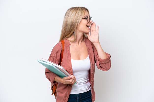 Zdjęcie piękna studentka blondynka izolowana na białym tle krzycząc z otwartymi ustami na bok