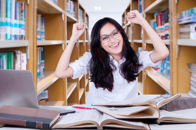 Piękna studentka podnosi ręce w bibliotece.