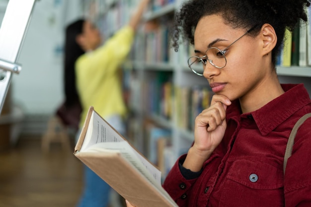 Piękna studentka spędza przerwę w bibliotece uniwersyteckiej, szukając potrzebnej lekcji literatury Studiowanie książek w koncepcji biblioteki