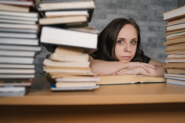 Piękna studentka studiująca z dużą ilością papierowych książek na stole