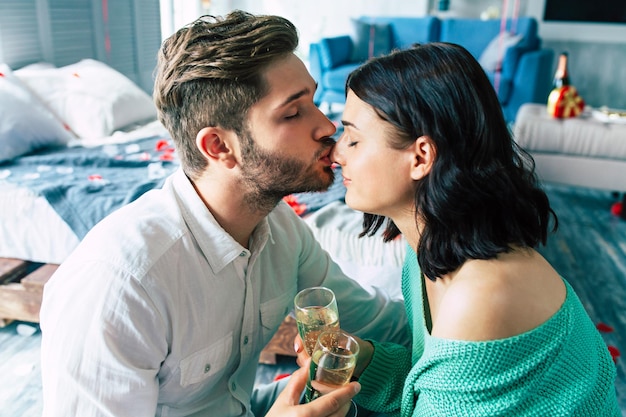 Piękna stylowa i urocza romantyczna młoda para przytula się do siebie, całuje i pije szampana, świętując jakąś randkę lub św. Walentynki w domu