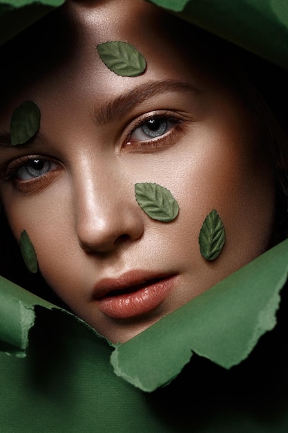 Zdjęcie piękna świeża dziewczyna z idealną skórą, naturalnym makijażem i zielonymi liśćmi piękna twarz zdjęcie zrobione w studio