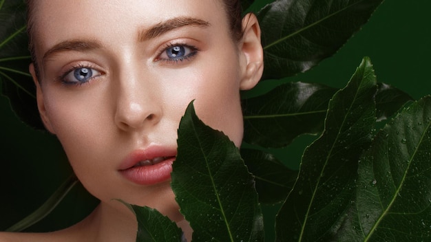 Piękna świeża dziewczyna z idealnym naturalnym makijażem skóry i zielonymi liśćmi Piękna twarz