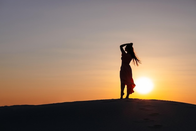 Piękna sylwetka dziewczyny na pustyni o zachodzie słońca