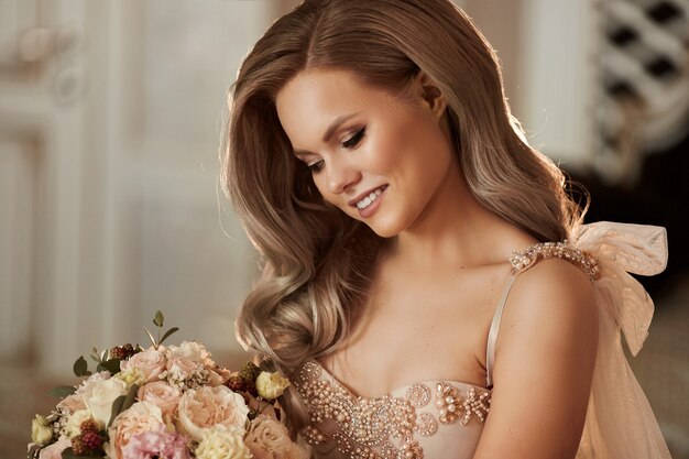 Piękna szczęśliwa blondynka modelka z uroczym uśmiechem w stylowej sukience z bukietem kwiatów w dłoniach