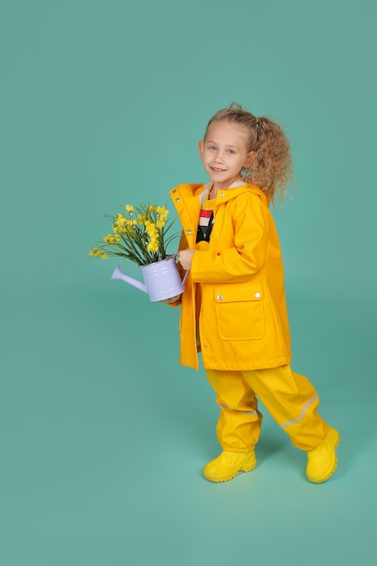 piękna szczęśliwa blondynka w żółtym kombinezonie i płaszczu przeciwdeszczowym trzyma wiadro kwiatów