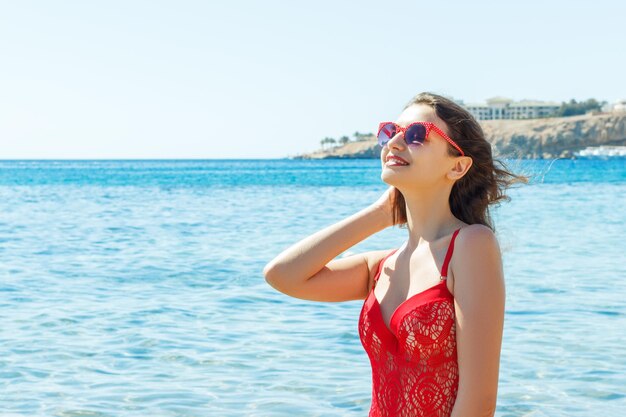 Piękna szczęśliwa brunetka dziewczyna pozuje na plaży w czerwonym kostiumie kąpielowym