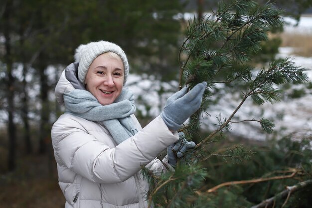 Piękna szczęśliwa dorosła starsza starsza emerytka staruszka z choinką w zimowym lesie baw się dobrze i uśmiechaj się i ciesz się śniegiem zabiera choinkę do domu z lasu