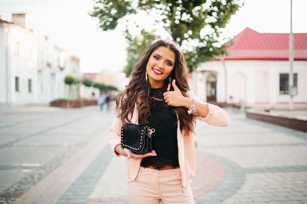 Piękna szczęśliwa dziewczyna z modną czarną torebką pokazuje kciuk up.