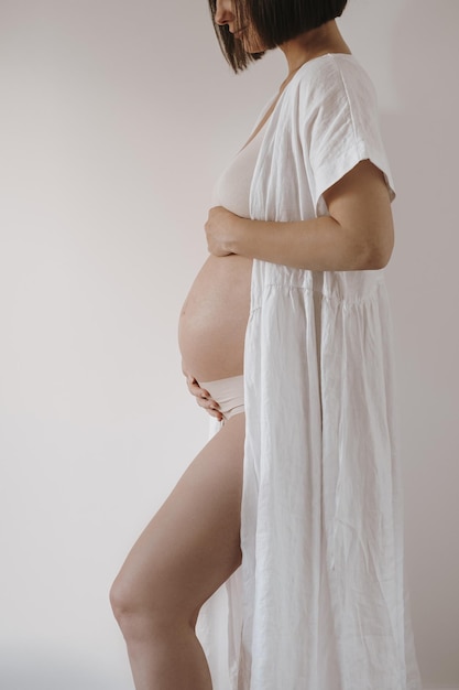 Piękna szczęśliwa kobieta w ciąży w eleganckiej białej szacie dotykająca brzucha Estetyczna elegancka ciąża macierzyński noworodek spodziewa się koncepcji