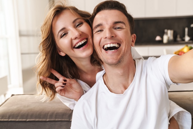 Piękna szczęśliwa młoda para relaksuje się na kanapie w salonie, biorąc selfie