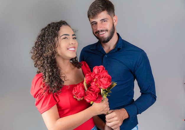 Piękna szczęśliwa para pozytywna przytula się patrząc na siebie trzymając bukiet czerwonych róż na szarym tle Walentynki