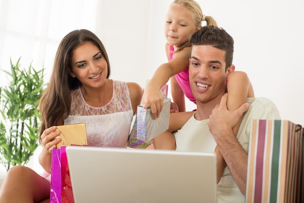 Piękna szczęśliwa rodzina siedzi w domu z laptopem i torbami na zakupy.