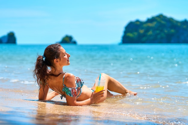Piękna szczupła dziewczyna w kostiumie kąpielowym cieszy się opalenizną leżąc na tropikalnej plaży