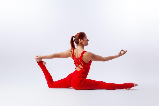 Piękna szczupła kobieta w sportowym kombinezonie uprawiająca jogę stojąca w pozie równoważenia asany na białym, izolowanym tle Koncepcja sportu i medytacji Trening rozciągania i jogi