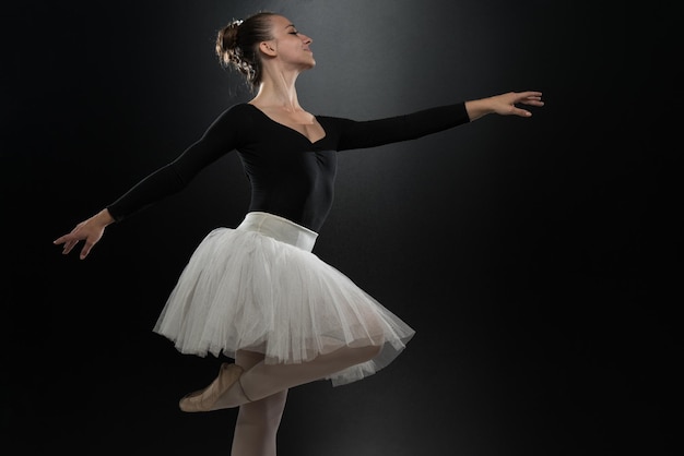 Piękna tancerka baletowa na czarnym tle Balerina ma na sobie tutu i buty pointe