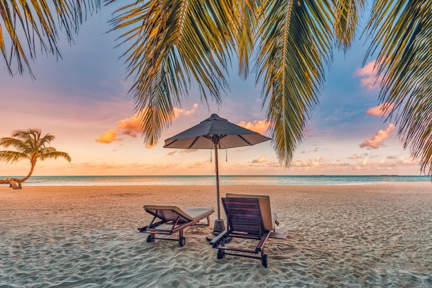 Piękna tropikalna plaża o zachodzie słońca. Romantyczna para goli dwa leżaki, parasol pod liśćmi palmy