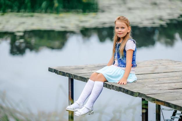 Piękna uczennica siedzi na brzegu jeziora lub rzeki na drewnianym molo z wiszącymi nogami