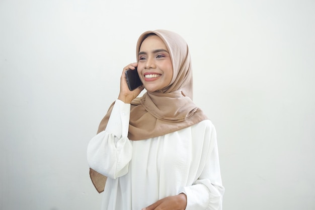 Piękna uśmiechnięta azjatycka muzułmańska kobieta nosi hidżab przy użyciu telefonu komórkowego na białym tle