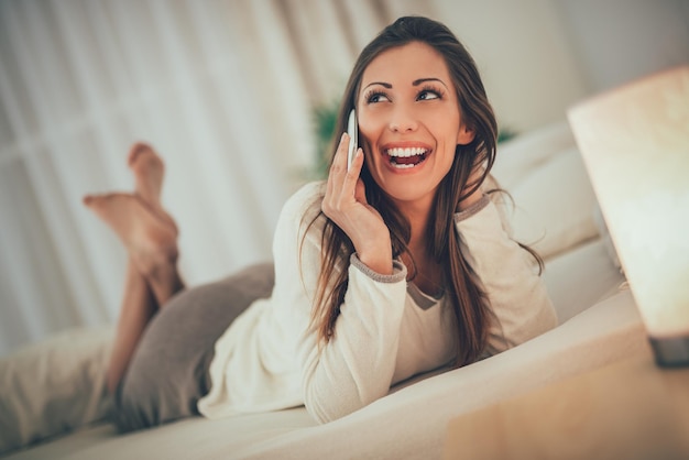 Piękna Uśmiechnięta Dziewczyna Relaks W łóżku I Przy Użyciu Telefonu Komórkowego.