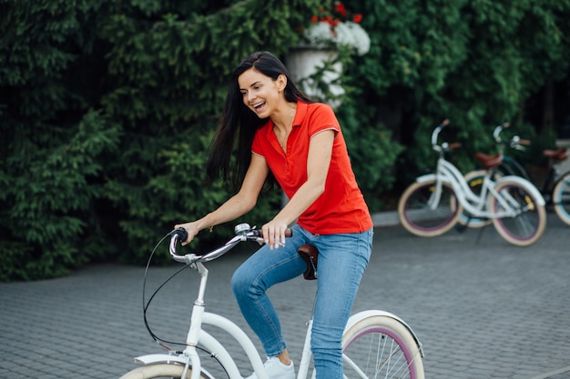 Piękna uśmiechnięta dziewczyna w czerwonej koszulce jedzie białego bicykl