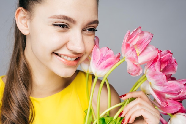 Piękna uśmiechnięta dziewczyna w żółtej sukience raduje się wiosną, trzyma bukiet pachnących różowych kwiatów