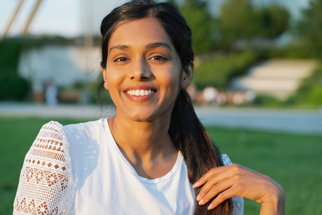 Piękna uśmiechnięta Indianka patrząc na kamery siedząc w parku. Koncepcja naturalnego piękna