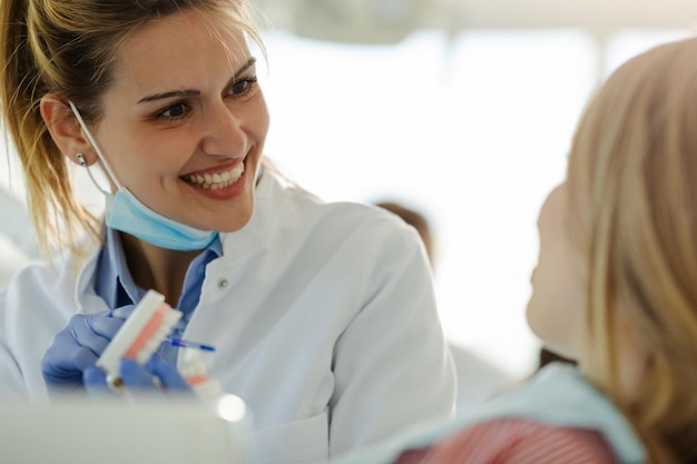 Piękna uśmiechnięta kobieta dentysta pokazując pacjentowi dziewczyna, jak prawidłowo myć zęby.