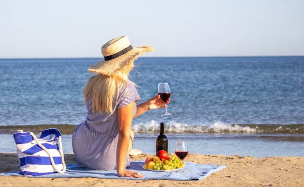 Piękna uśmiechnięta kobieta przy lampce wina na plaży. Czerwone wino owocowe.