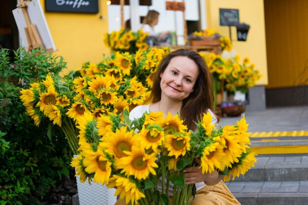 Piękna uśmiechnięta kobieta z jasnożółtymi słonecznikami w pobliżu kawiarni - kwiaciarnia