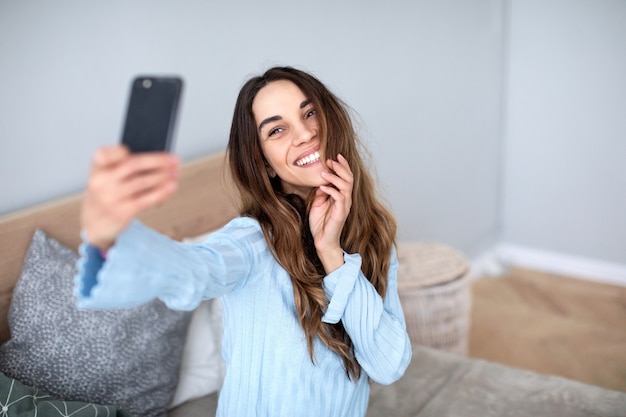 Piękna uśmiechnięta kobieta z telefonem robi selfie w domu. Styl życia.