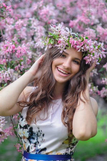 Piękna uśmiechnięta kobieta z wiankiem w kwitnącym wiosna ogródzie