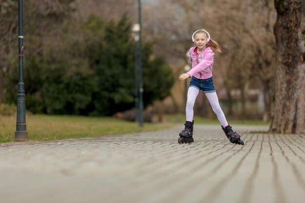 Piękna uśmiechnięta mała dziewczynka na rolkach po parku.