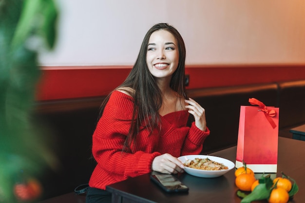 Piękna uśmiechnięta młoda azjatycka kobieta w czerwonych ubraniach je azjatyckie jedzenie w chińskiej restauracji