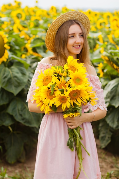 Piękna uśmiechnięta młoda kobieta w białej koszula stoi w polu wśród słoneczników