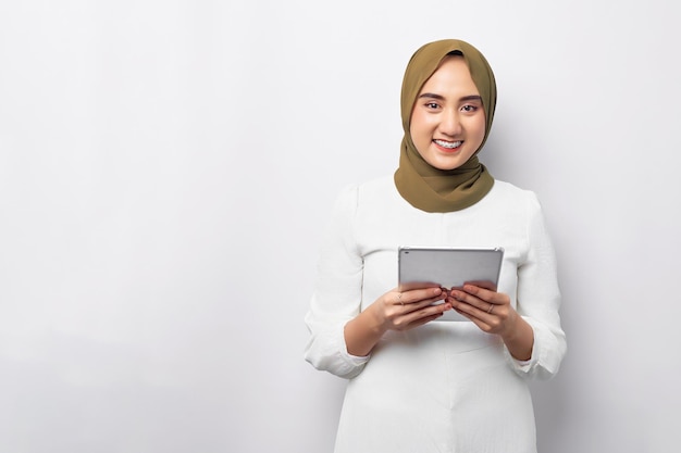 Piękna uśmiechnięta przyjazna młoda arabska azjatycka muzułmanka ubrana w zielony hidżab trzymająca cyfrowy tablet patrząc na kamerę odizolowaną na białym tle Koncepcja religijnego stylu życia ludzi